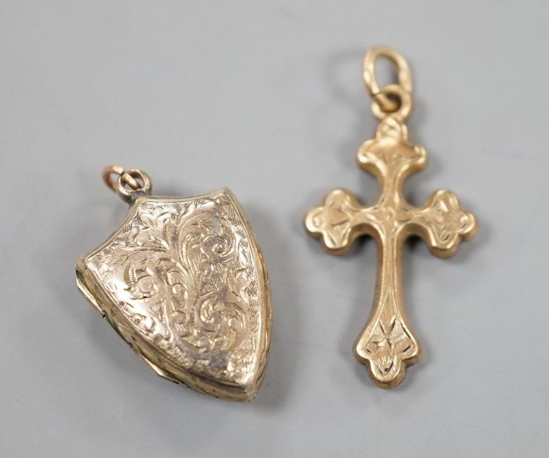 A 9ct gold cross pendant charm, 21mm and a similar engraved yellow metal shield shaped locket charm